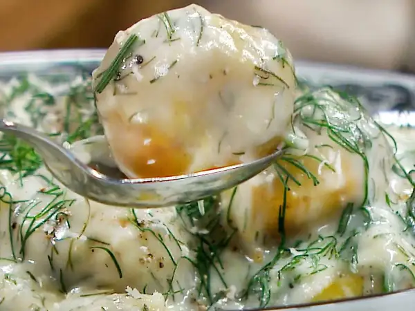 En sked lyfter upp en bit krämig dillstuvad potatis, täckt av färsk dill och en len sås.