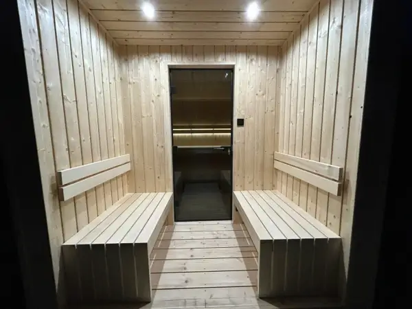 Drewniana sauna z ławami i szklanymi drzwiami. Dyskretna wentylacja w saunie zapewnia komfort.