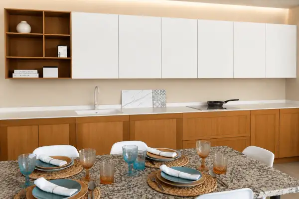 Elegantes cocinas modernas blancas con gabinetes de madera, encimera de cuarzo y mesa lista para cenar.