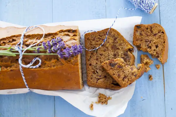 Pokrojony chlebek bananowy z gałązką lawendy i sznurkiem na niebieskim tle.