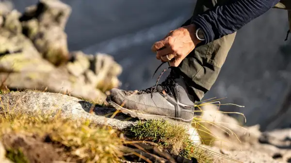 Mężczyzna sznuruje buty trekkingowe na kamieniu. Czy buty trekkingowe powinny być większe? Odpowiedź tkwi w komforcie i ochronie palców.