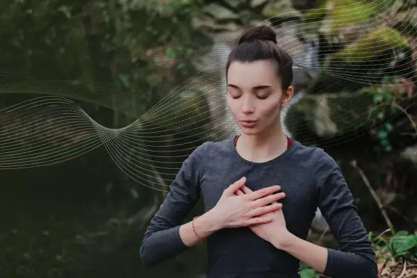 Kobieta z zamkniętymi oczami praktykuje techniki oddychania pranayama na tle natury.