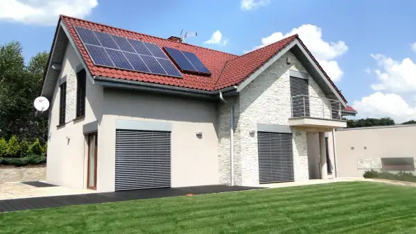 Nowoczesny dom z panelami solarnymi na dachu, otoczony zielonym ogrodem.