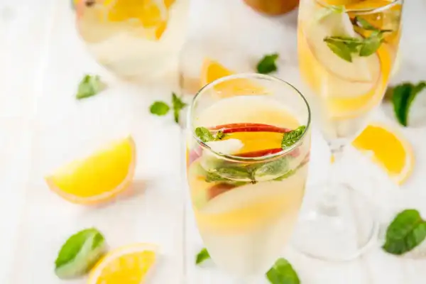 Verre de sangria blanche garni de tranches de pomme, d'orange et de menthe fraîche. Parfait pour une journée ensoleillée.