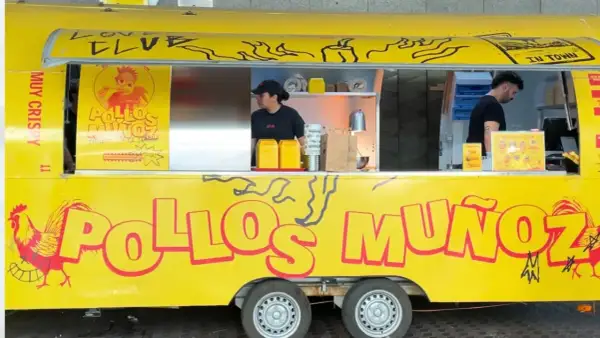 Camión amarillo "Pollos Muñoz" con un gallo rojo. Dos empleados trabajan en el interior.