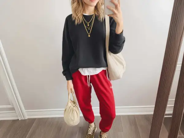 Styling-Idee: Schwarzer Pullover, weiße Schicht, rote Hose mit weißen Streifen, Leo-Sneaker und cremefarbene Taschen. Perfekt, wenn du fragst, was passt zu roter Hose!