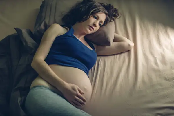 Zmęczona kobieta w zaawansowanej ciąży leży na łóżku, próbując zasnąć. Bezsenność w ciąży to częsty problem.