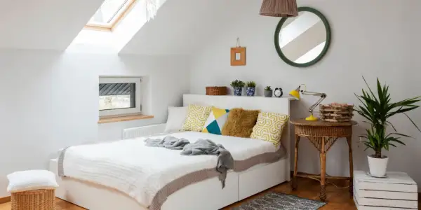 Chambre sous pente lumineuse avec lit blanc, coussins géométriques, et un puits de lumière. Une belle idée peinture pour un espace cosy.