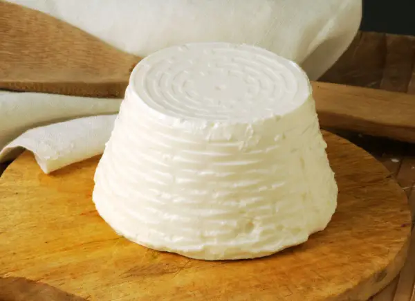 Świeży serek ricotta o stożkowatym kształcie, z charakterystycznym wzorem na wierzchu, leży na drewnianej desce.