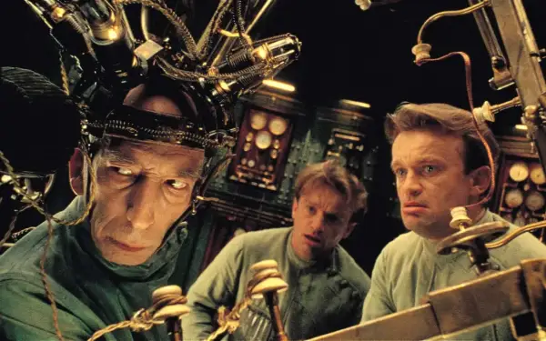 Trzej mężczyźni w dziwnych hełmach, jak z **starych filmów science fiction**, pracują przy skomplikowanej maszynie.