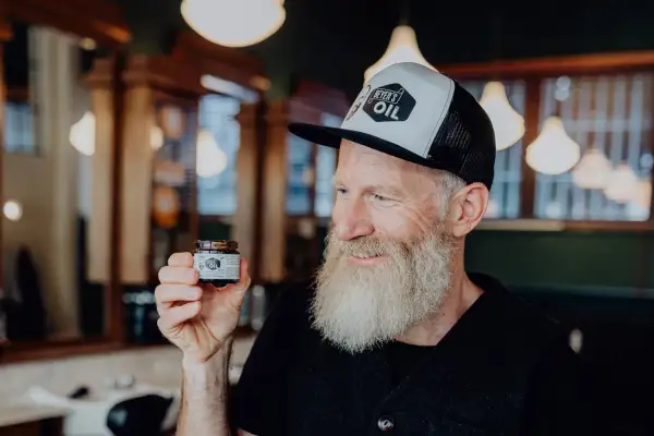 Mann mit Bart hält Tiegel "Beyer's Oil". Perfekt für Bartpflege selber machen.