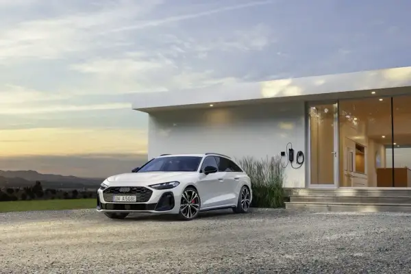 Białe Audi A6 Avant TFSI, zaparkowane przed nowoczesnym domem z ładowarką.