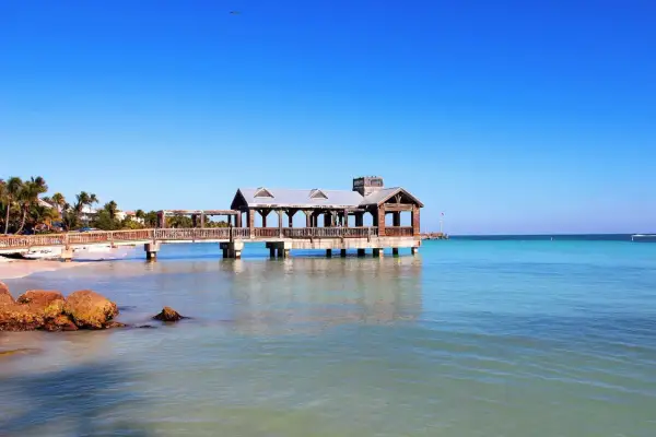 Un ponton en bois avec un kiosque, typique du parc Key West, s'avance sur une mer turquoise sous un ciel bleu éclatant.