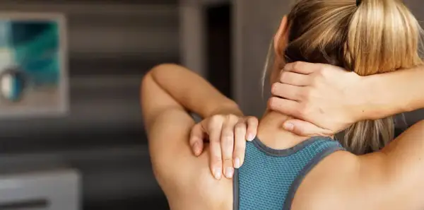 Une femme se masse le cou, peut-être pour soulager une douleur ou pour muscler son cou après un entraînement.