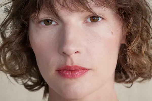 Zbliżenie na twarz kobiety z brązowymi oczami i falowanymi włosami. Retinol dla kogo? Dla każdej kobiety pragnącej odmłodzonej skóry.