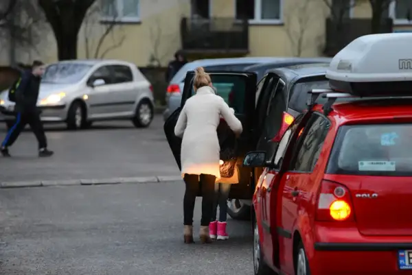 Kobieta z dzieckiem wsiada do samochodu, tworząc zator. Miejsce, gdzie nie można parkować, bo blokuje ruch.