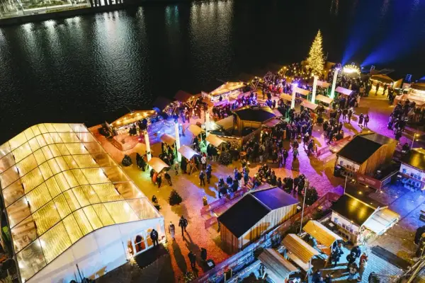 Buntes Treiben auf einem weihnachtsmarkt an der Spree. Menschen schlendern zwischen beleuchteten Buden und einem großen Weihnachtsbaum.
