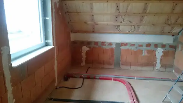 Neue Heizungsrohre verlegen im Rohbau. Rote und graue Rohre liegen auf dem Boden, bereit für die Installation.