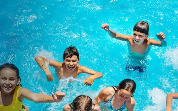 Niños riendo y chapoteando en una piscina azul, disfrutando del verano. ¡Una imagen perfecta de campamentos de inglés en España!