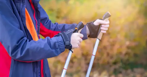 Osoba w kurtce przygotowuje się do marszu, trzymając kijki trekkingowe. Poznaj, jak chodzić z kijkami trekkingowymi, by czerpać z tego maksimum korzyści.