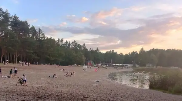 Plaża nad jeziorem w Jelczu-Laskowicach tętni życiem. Ludzie odpoczywają na piasku, kąpią się w wodzie, a dzieci bawią się przy dmuchanych zjeżdżalniach.