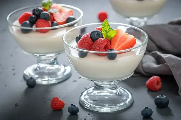 Två glas med krämig panna cotta, toppad med färska bär som jordgubbar, hallon och blåbär. En perfekt dessert.