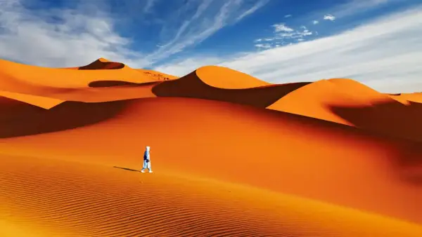 Un voyageur solitaire traverse la majestueuse dune du Sahara sous un ciel bleu éclatant.
