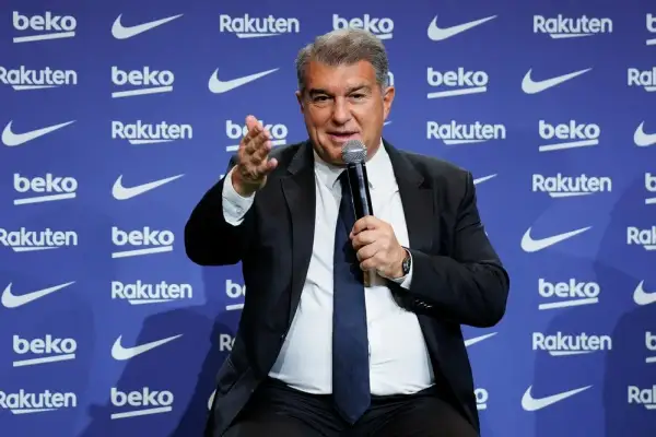 Joan Laporta, właściciel Barcelony, przemawia do mikrofonu na tle niebieskiej ściany z logo sponsorów klubu.