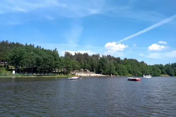 Spokojne jezioro Stobno otoczone zielonym lasem, z plażą i kilkoma łodziami.