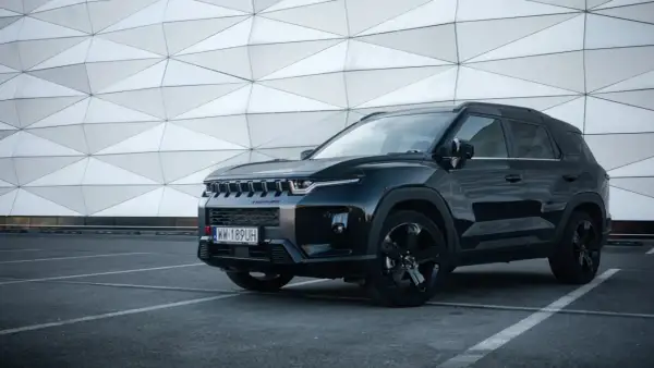 Czarny SsangYong Torres z czarnymi felgami stoi na parkingu przed nowoczesnym budynkiem o geometrycznej fasadzie.