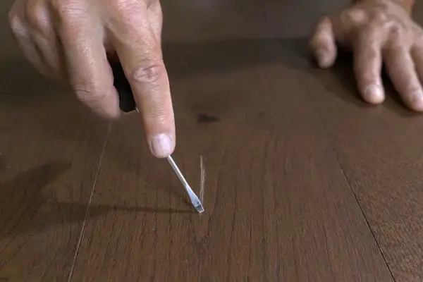 Mano che usa un cacciavite per sistemare parquet graffiato, un piccolo ritocco per un pavimento perfetto.