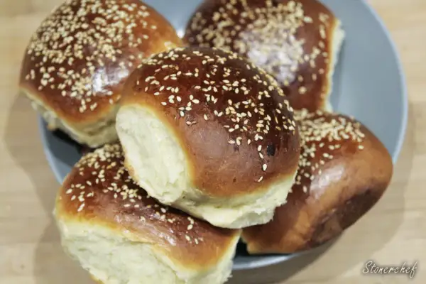 Pięć puszystych bułek do burgerów, posypanych sezamem, ułożonych na talerzu. Idealne na domowe burgery.