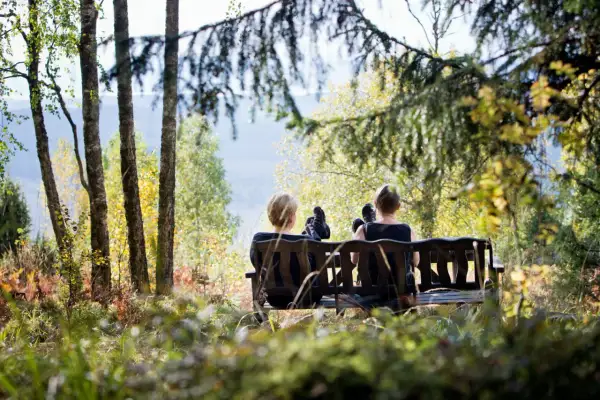 Två personer vilar på en bänk under en **weekend vandring i Sverige**. Höstfärger och solljus lyser upp skogen.