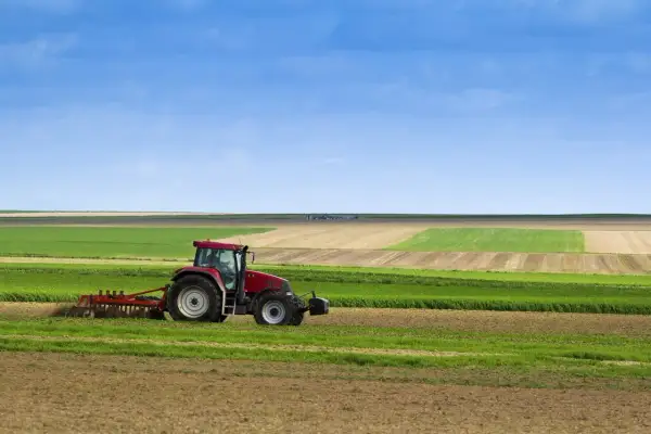 Tracteur rouge travaillant dans un champ, préparant le sol pour le semis direct. Paysage agricole sous un ciel bleu.