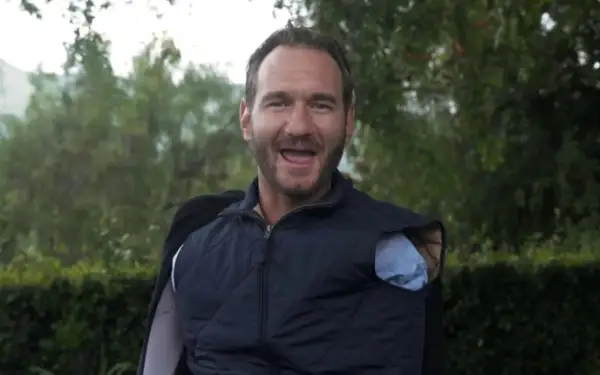 Nick Vujicic, lächelnd und mit offenem Mund, trägt eine blaue Weste über einem Hemd.