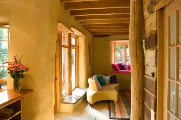Interno accogliente con pareti in intonaco terra cruda, mobili in legno grezzo e un divano giallo con cuscini colorati.