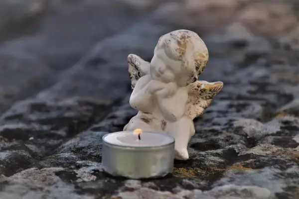 Aniołek czuwa przy płonącej świecy, symbolizując pamięć i żal po śmierci bliskiej osoby.