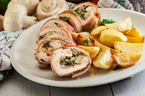 Roladki z kurczaka zawinięte w boczek, podane z pieczonymi ziemniakami i ziołami.