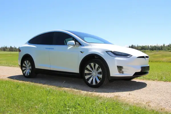 Biała Tesla Model X na tle zielonej łąki i lasu. Zastanawiasz się, ile kosztuje Tesla?