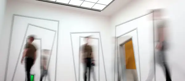 Mensen bewegen door een gang met geometrische openingen, wat een indruk geeft van een sensorische informatieverwerking test.