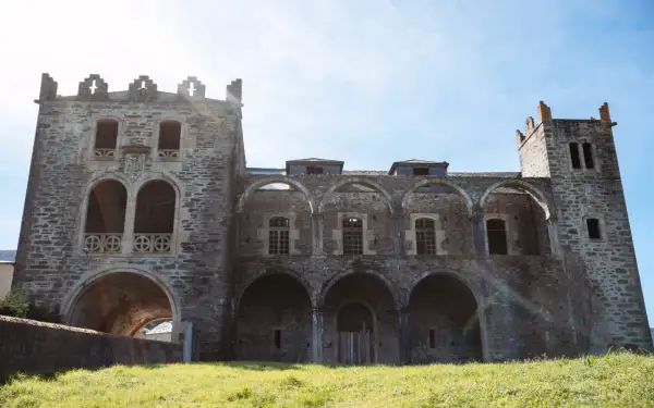 El imponente castillo de Arnado, con sus arcos y torres de piedra, se alza sobre un prado verde bajo un cielo azul.