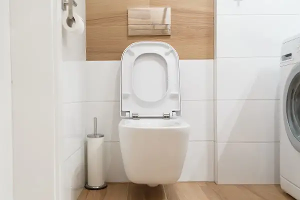 Cassetta a muro WC perde acqua, un problema comune in bagno. Si vede il water sospeso, il rotolo di carta igienica e la lavatrice.