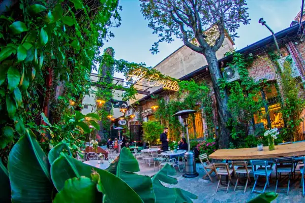 Un cortile rigoglioso ospita aperitivi milanesi particolari. Tavoli all'aperto, luci soffuse e vegetazione creano un'atmosfera magica.