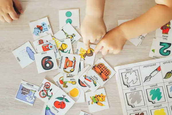 Manos de niños jugando con tarjetas de aprendizaje, practicando ejercicios de memoria con imágenes de animales, números y objetos.