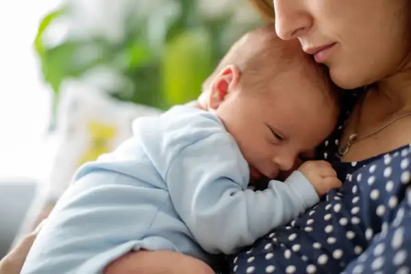 Mutter hält ihr schlafendes Baby. Der leichte baby haarausfall ist kaum sichtbar, während das Kind friedlich an ihrer Brust ruht.