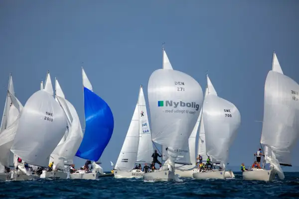 Regata con spinnaker gonfiati, tra cui uno blu acceso e uno bianco con logo Nybolig. Le barche competono in una giornata di sole.