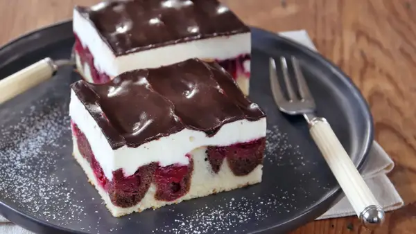 Zwei Stücke saftige Donauwelle mit Kirschen, weißer Creme und Schokoladenguss auf einem Teller. Ein köstliches Donauwelle Rezept!