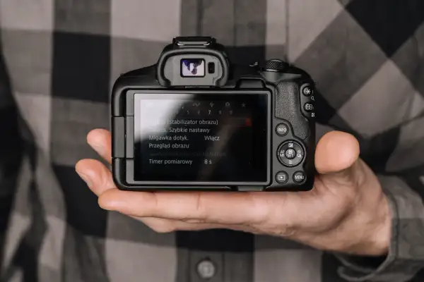 Dłoń trzyma aparat, na ekranie menu. Minimalizm w fotografii to sztuka uchwycenia esencji.