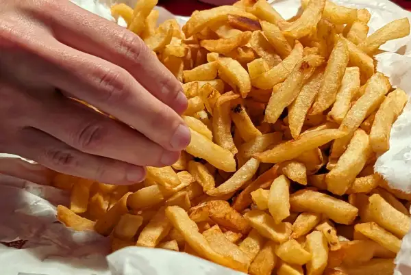 En hand plockar en gyllene pommes frites ur en stor hög med krispiga pommes frites.