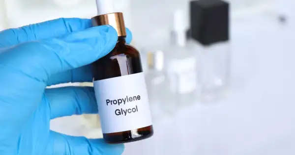 Ręka w niebieskiej rękawiczce trzyma buteleczkę z etykietą "Propylene Glycol".